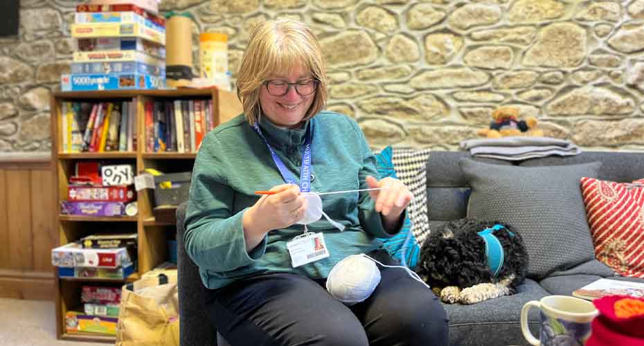 Older woman sat on sofa knitting with dog next to her in chaplaincy stone building