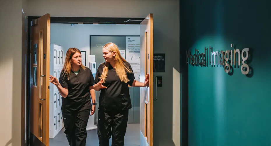 Two students wearing scrubs walking through the double doors to the Medical Imaging Unit