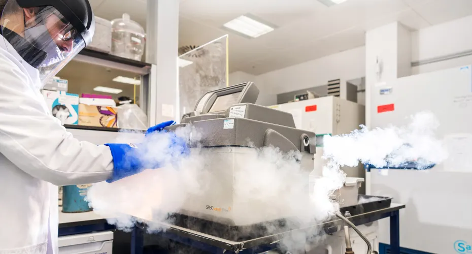 A student in a lab coat operates a machine that produces smoke in a laboratory setting.