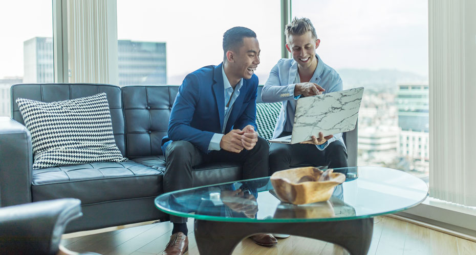 Two business people sitting on a couch, smiling at a laptop