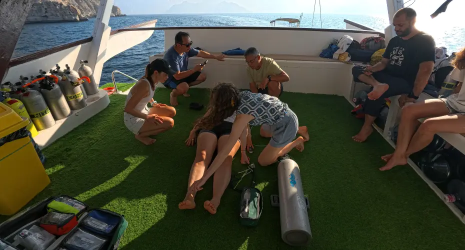 Group of Extreme Medicine students on a dive boat. One student is acting as a demo patient, receiving treatment on their foot.