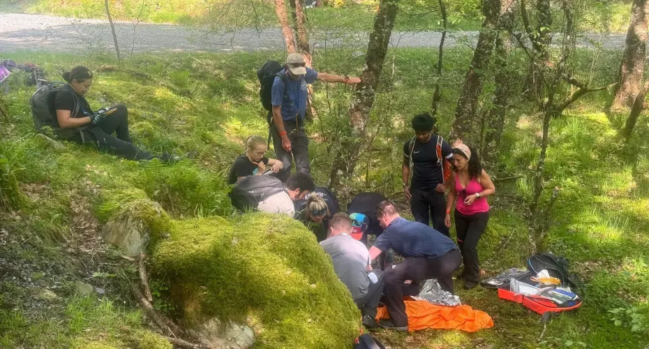 Group of Extreme Medicine students on a Core Concepts residential in the UK. Students are treating a demo patient in a woodland area outside.