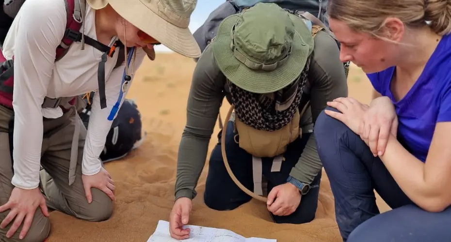 Three Extreme Medicine students in the desert kneeling down looking at map and using compass