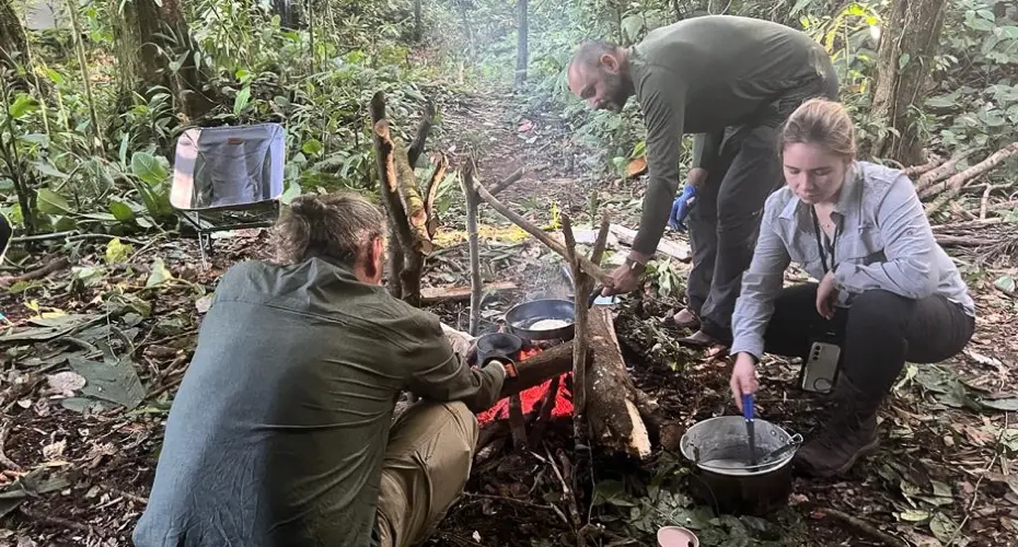 Three Extreme Medicine students in a rainforest environment, cooking food over a basic stove made with sticks