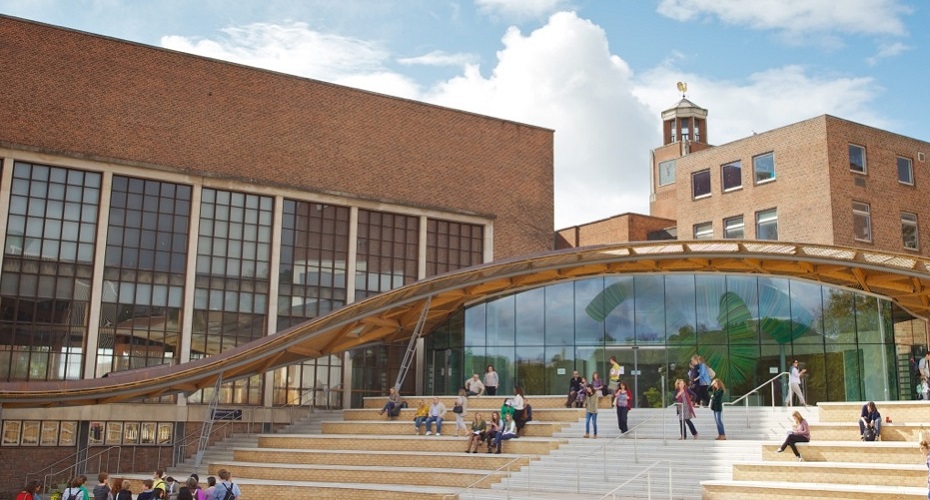 Individuals walking on the steps of the great hall at the university of exeter, highlighted by a modern curved glass roof.