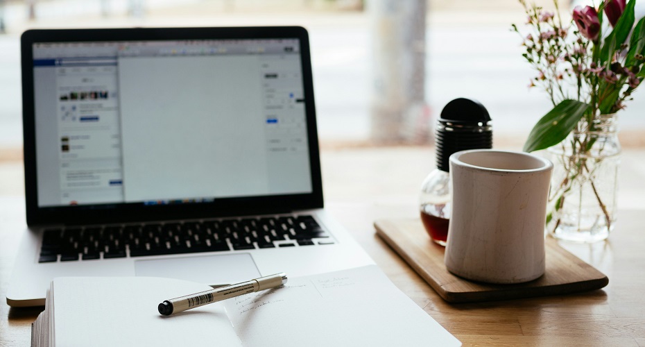 A laptop on a desk next to an open notebook